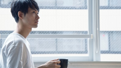 窓辺でコーヒーを飲む男性のイメージ写真。お客様本人ではありません